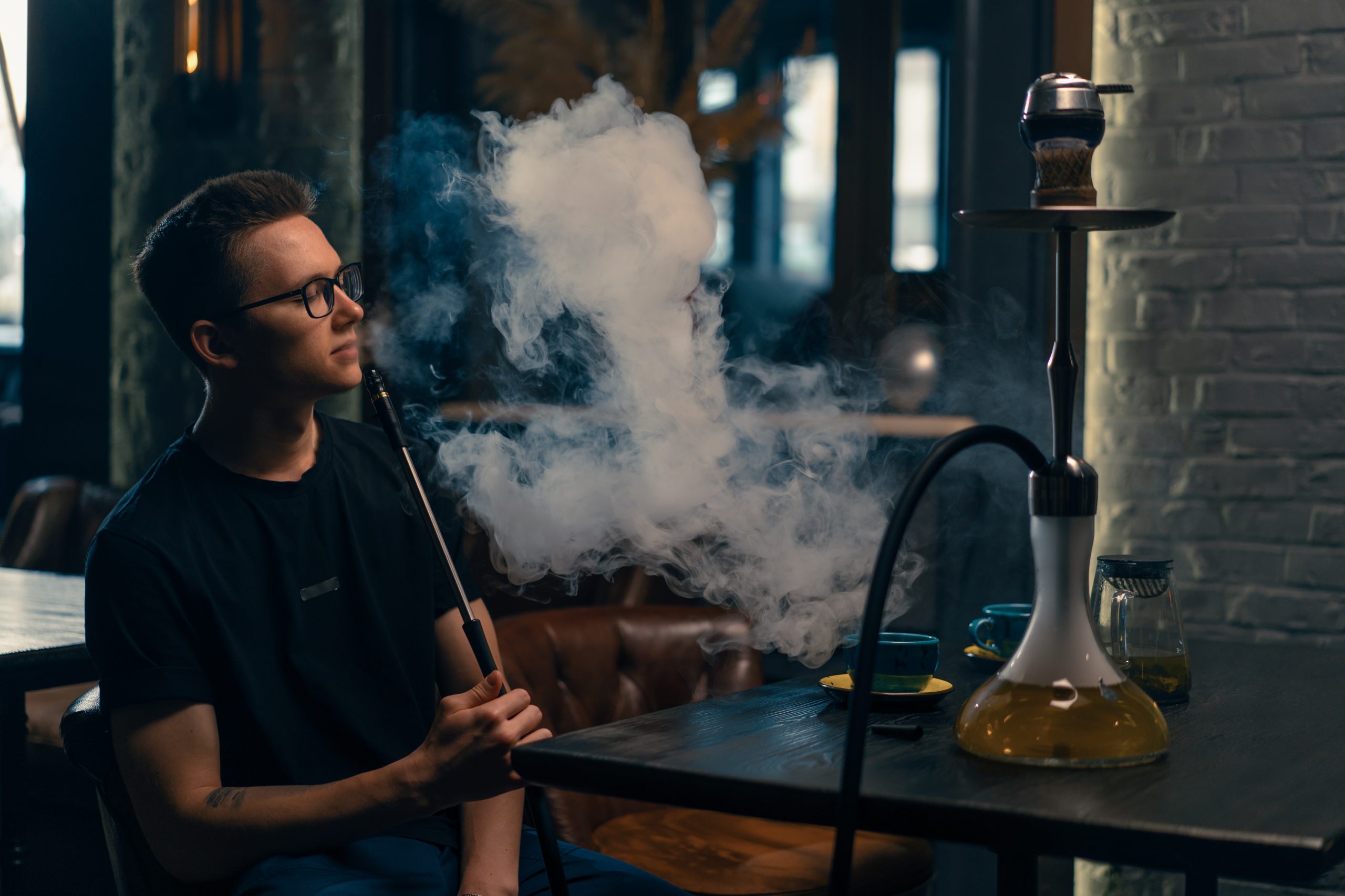 A man in glasses smokes a traditional hookah pipe A man exhales thick smoke in a hookah cafe or lounge bar